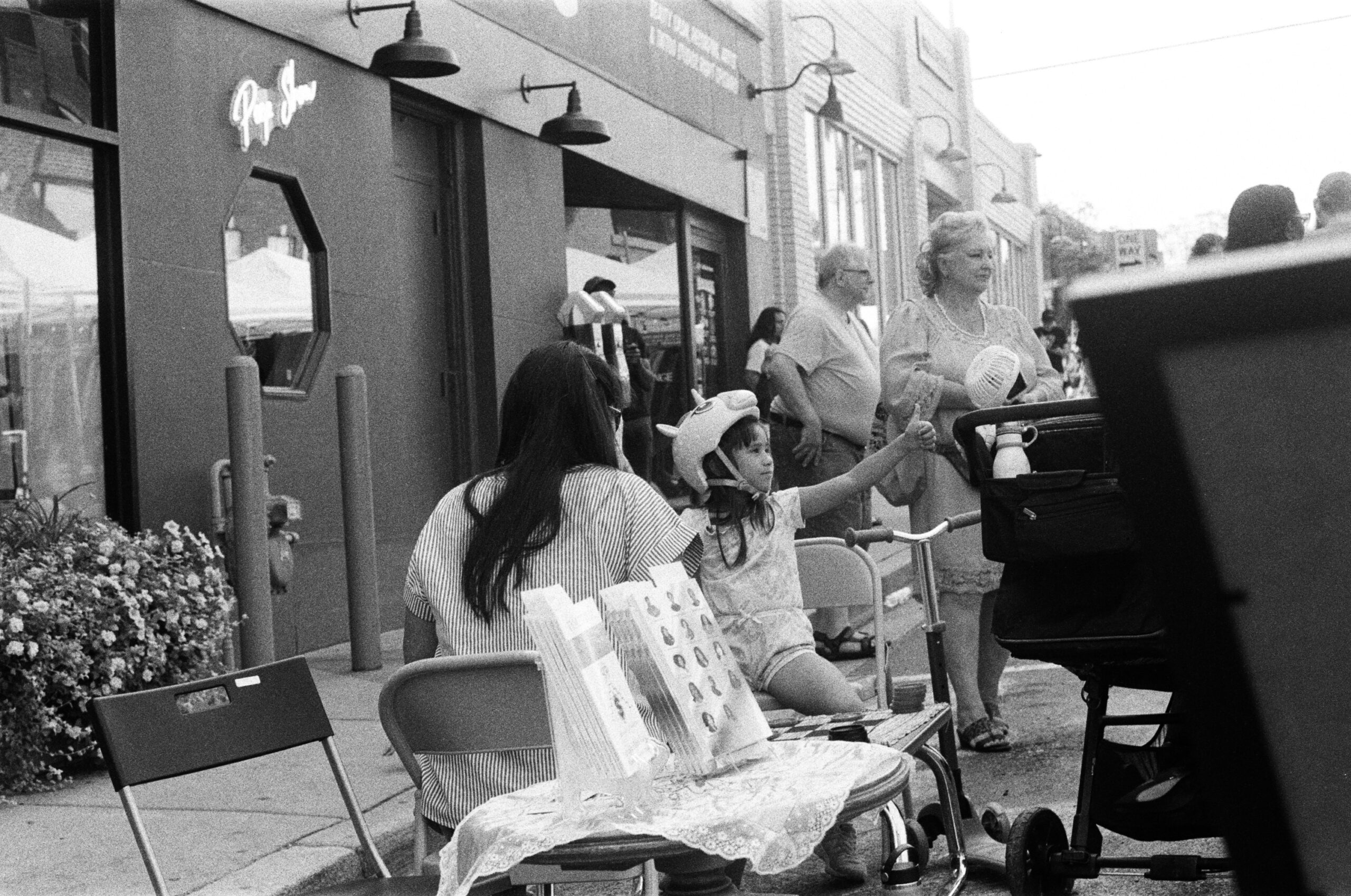 A group of people on the street looking at the same thing; a girl with a helmet on gives a thumbs up.