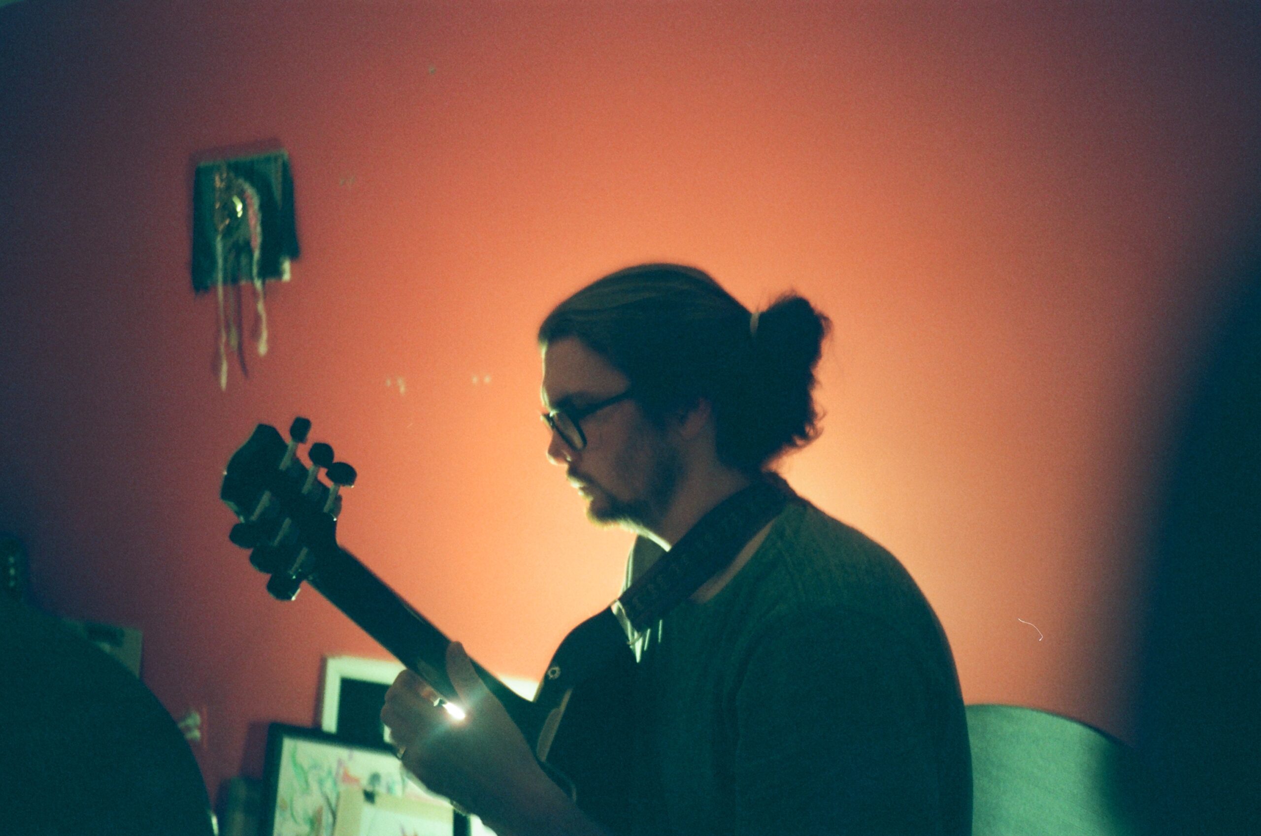 Person with guitar sits in front of a back-lit orange wall
