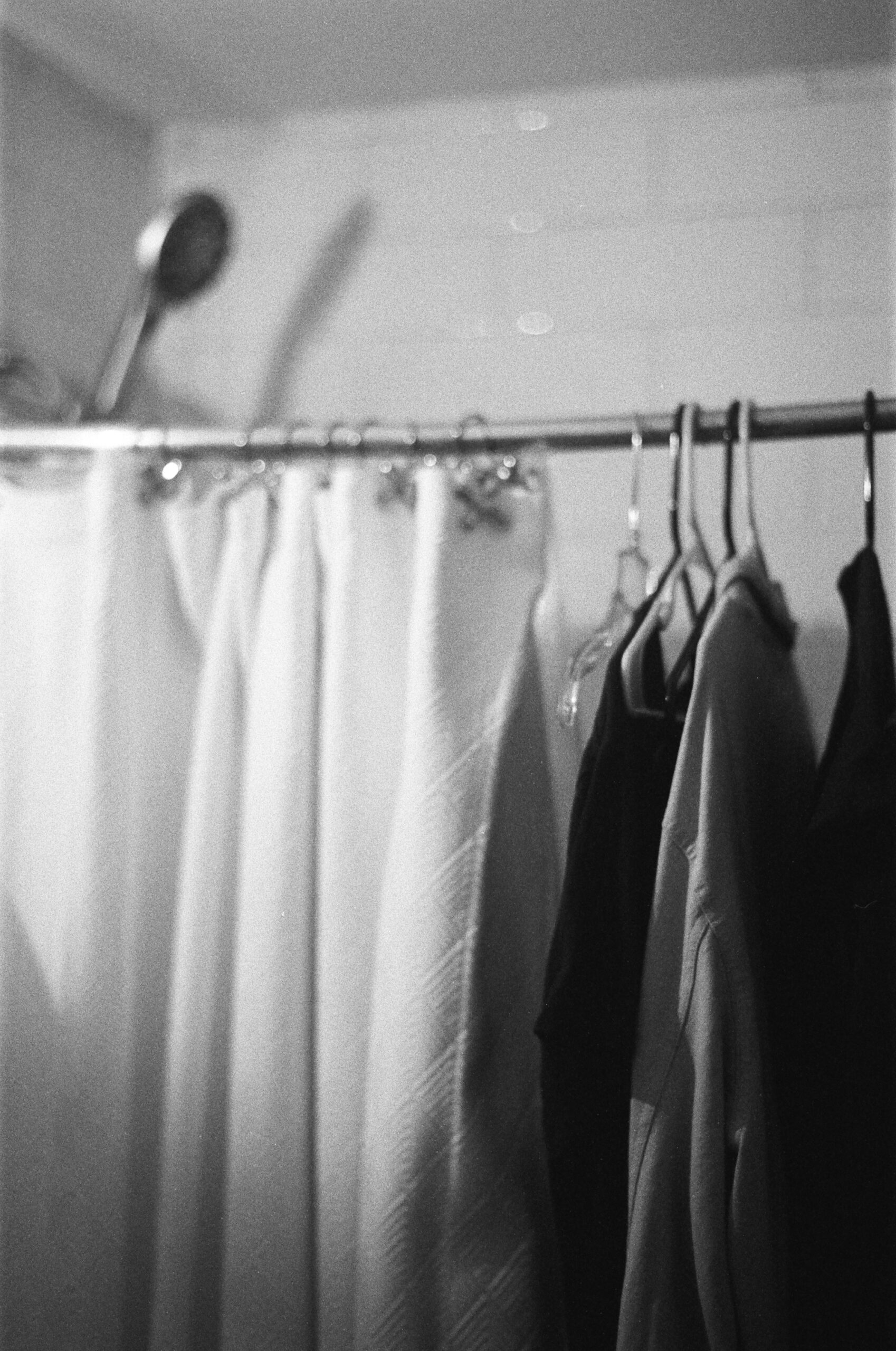 Clothes hang from a shower-curtain-rod next to some shower curtains.