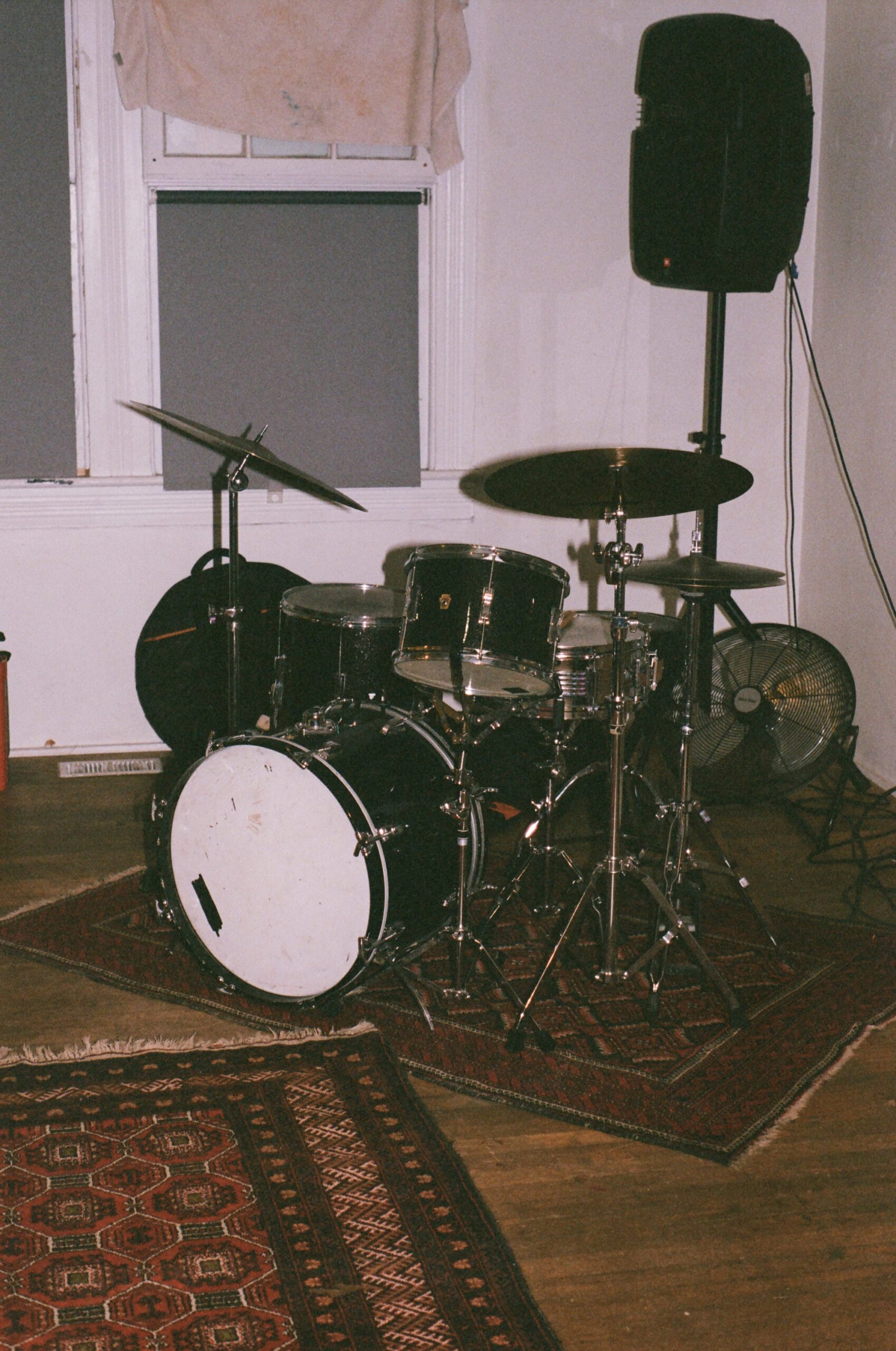 A drum set sits in front of a white wall next to a tall speaker